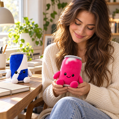 Pink and blue energy drink can plush toys in a cosy home workspace